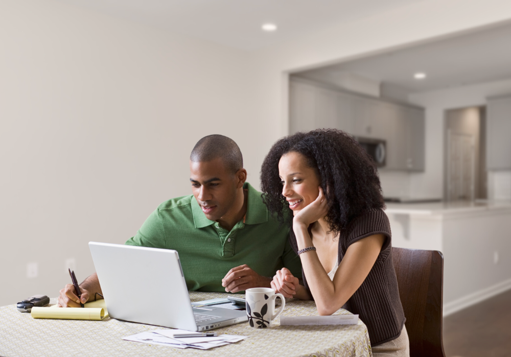 A man and woman at a table look at the screen of a laptop computer.